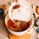 Person adding spices to a pot on a kitchen counter