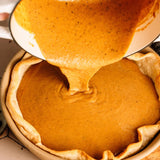 Pumpkin pie filling being poured into a pie crust
