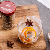 Glass of cocktail with star anise and orange slices on a wooden board with a jar of star anise.