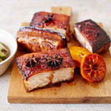 Sliced roasted pork belly on a wooden board with a halved lime and small bowl of dipping sauce.