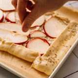 Hand placing apple slices on a pastry dish with a hand holding a piece of apple.