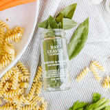Bottle of Bay Leaves with pasta and leaves on a textured surface