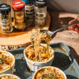 Spoon lifting pasta from a small dish with spices in the background