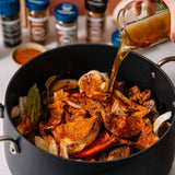Spices being poured into a pot with vegetables on a kitchen counter