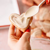 Heart-shaped cookie being filled with cream using a spoon.