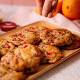 Cookies with red chips on a wooden tray, with a hand reaching towards them.