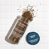 Jar of caraway seeds with scattered seeds on a white background
