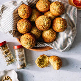 Bowl of muffins with ground flaxseed and chia seed containers on a speckled surface.