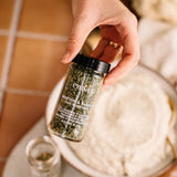Hand holding a jar of chive seasoning with a blurred background