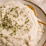 Mashed potatoes with green herbs in a bowl with a gold spoon