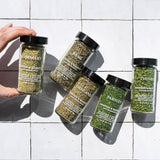 Five jars of dried herbs on a tiled surface