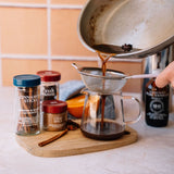 Pouring coffee from a pot through a filter into a glass carafe on a kitchen counter.