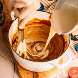 Person stirring a pot of brown sauce with a whisk, with a bottle of Star Anise visible.
