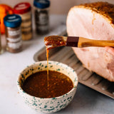 Wooden brush dipping into a bowl of brown sauce with a roasted turkey in the background.