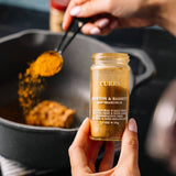 Hand holding a jar of Morton & Bassett Curry powder with a pan in the background.