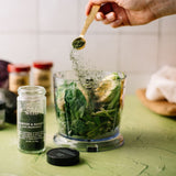 Person adding spices to a blender with ingredients on a kitchen counter