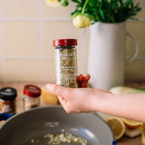 Hand holding a jar of fennel seed with a kitchen background