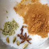 Spices including cumin, fennel seeds, star anise, and cardamom on a white surface.