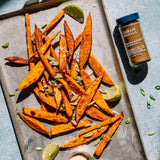 Baked sweet potato fries on a baking tray with a jar of cajun seasoning.