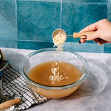 Person adding ingredients to a bowl of liquid on a kitchen counter.