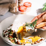 Person holding a piece of bread with a poached egg and herbs over a plate of similar food.