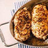 Two seasoned chicken breasts in a glass baking dish on a striped towel.