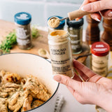 Person measuring ground ginger into a dish with various spices in the background