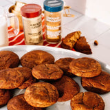Spiced cookies on a plate with ground ginger and cinnamon jars in the background.