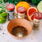Spices and a bowl of marinade on a surface with citrus and herbs in the background