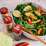 Salad with greens, avocado, and tomatoes in a bowl with spices on the side.