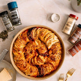 Baked dish with sliced potatoes on a table with seasoning bottles and utensils.