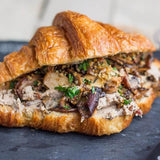 Sandwich with meat and mushroom filling on a croissant, on a dark surface.