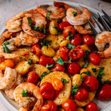 A dish featuring shrimp, potatoes, tomatoes, and herbs, arranged attractively on a white plate.