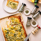 Zucchini tart with spiral toppings on a tray, surrounded by spice jars and a knife, ready for serving.