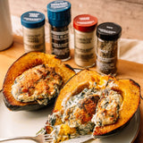 Two halves of roasted acorn squash stuffed with a creamy spinach and cheese filling, served on a plate with a fork, with four spice jars in the background on a wooden surface.