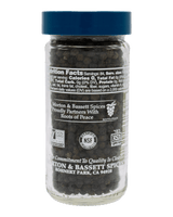 A clear glass spice jar filled with dark peppercorns, featuring a dark blue screw-top lid and a black label with white text. The label prominently displays the Morton & Bassett Spices brand name and logo, set against a solid black background.