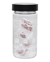A clear glass jar of Motion & Bassett Spices with a black lid, containing red and white whole spices, shown against a solid black background.