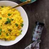 Yellow rice dish with saffron threads and a bottle of Morton & Bassett saffron threads on a wooden surface.