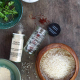 Spices and ingredients on a wooden surface including onion powder, fennel seeds, and rice.