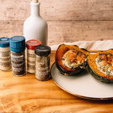 Seasoned ground turkey stuffed into halved acorn squash on a white plate, styled with spice jars and a white bottle on a wooden table.