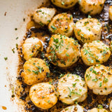 Pan-seared scallops garnished with chopped fresh parsley and herbs, cooking in a pan with a light cream-colored interior.