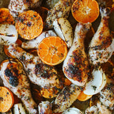 Roasted chicken with orange slices on a baking tray