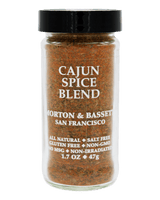 A clear glass spice jar filled with a brown-orange Cajun spice blend, topped with a black lid. The front label reads 'CAJUN SPICE BLEND' and shows the Morton & Basset San Francisco brand.