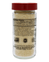 A clear plastic spice jar filled with light tan seasoning powder and topped with a red screw cap, shown against a black background. The back label is visible, showing Morton & Bassett Spices branding and nutrition facts.