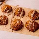 Five golden-brown cookies topped with white icing, arranged on parchment paper with a drizzle of icing being poured from the top.