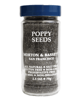 A jar of Morton & Bassett San Francisco Poppy Seeds on a solid black background. The clear glass jar shows the dark brown poppy seeds inside, with white text on the front label and a dark blue screw cap.