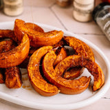 Roasted pumpkin pie filling slices on a white plate, drizzled with honey syrup, with blurred spice jars in the background.