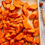 Roasted sweet potato wedges with a golden-brown crispy coating, scattered across a baking sheet lined with parchment paper.