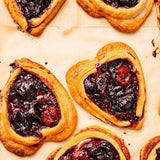 Heart-shaped berry pastries with golden-brown flaky pastry edges and dark red berry filling, arranged on parchment paper.