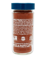 A clear glass spice jar filled with reddish-brown ground pepper or chili seasoning, topped with a blue screw cap. The front label shows nutrition facts, a 'Certified Gluten Free' seal, an NSF Certified Non-GMO product mark, and branding for Morton & Bassett Spices.